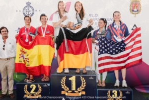 Esther und Luisa stehen bei der Siegerehrung auf dem Podium mit einer Deutschlandflagge in der Hand. Auf Platz zwei ein spanisches Team und auf Platz ein amerikanisches Team.